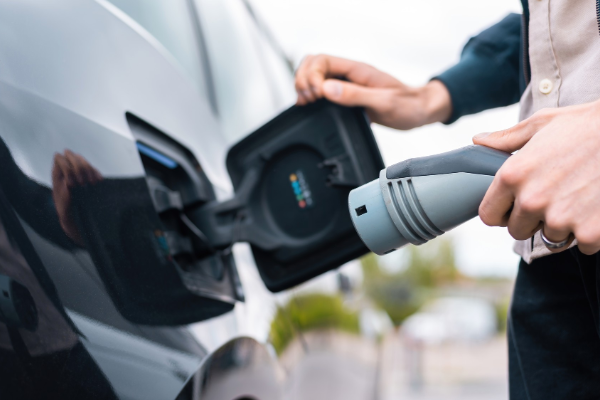 Man opening cars charge socket and holding charger at charge station