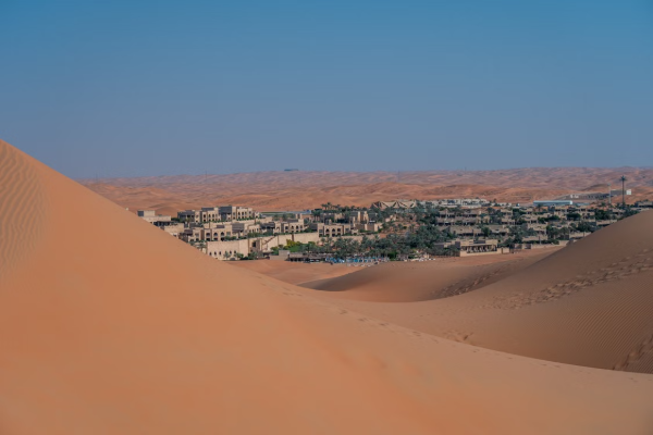 Scenic view of a liwa desert town nestled between vast sand dunes under a clear blue sky