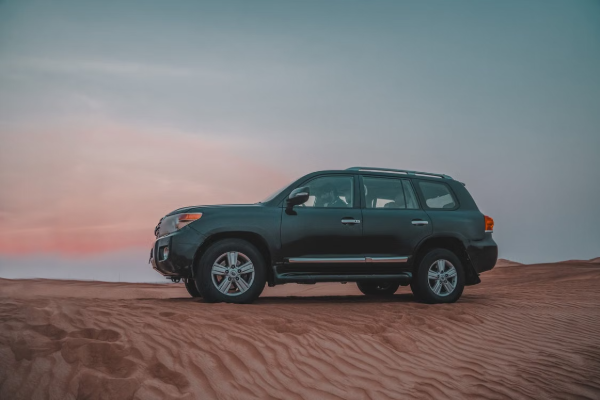 Side view of off-road SUV driving through desert dunes at twilight